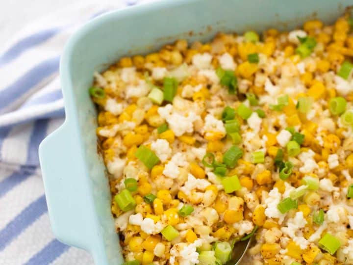 A blue baking dish with yellow Mexican Street Corn casserole has crumbled cheese and fresh green onions sprinkled over the top.