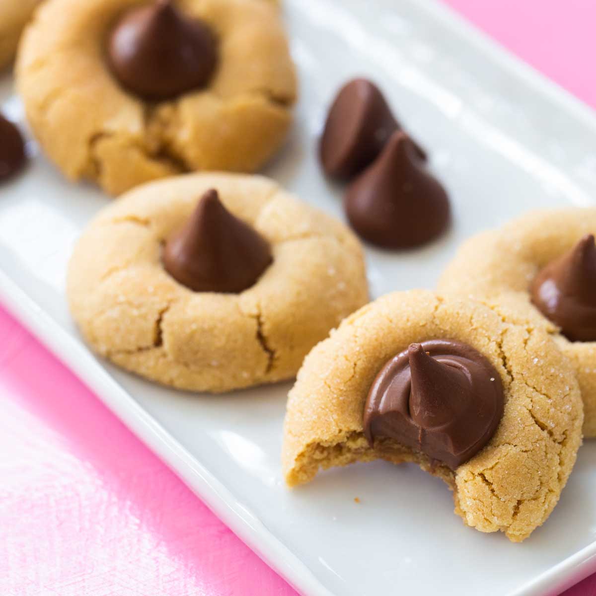 A platter of peanut butter blossom cookies have a Hershey kiss pushed into the top. The front one has a bite out of it.