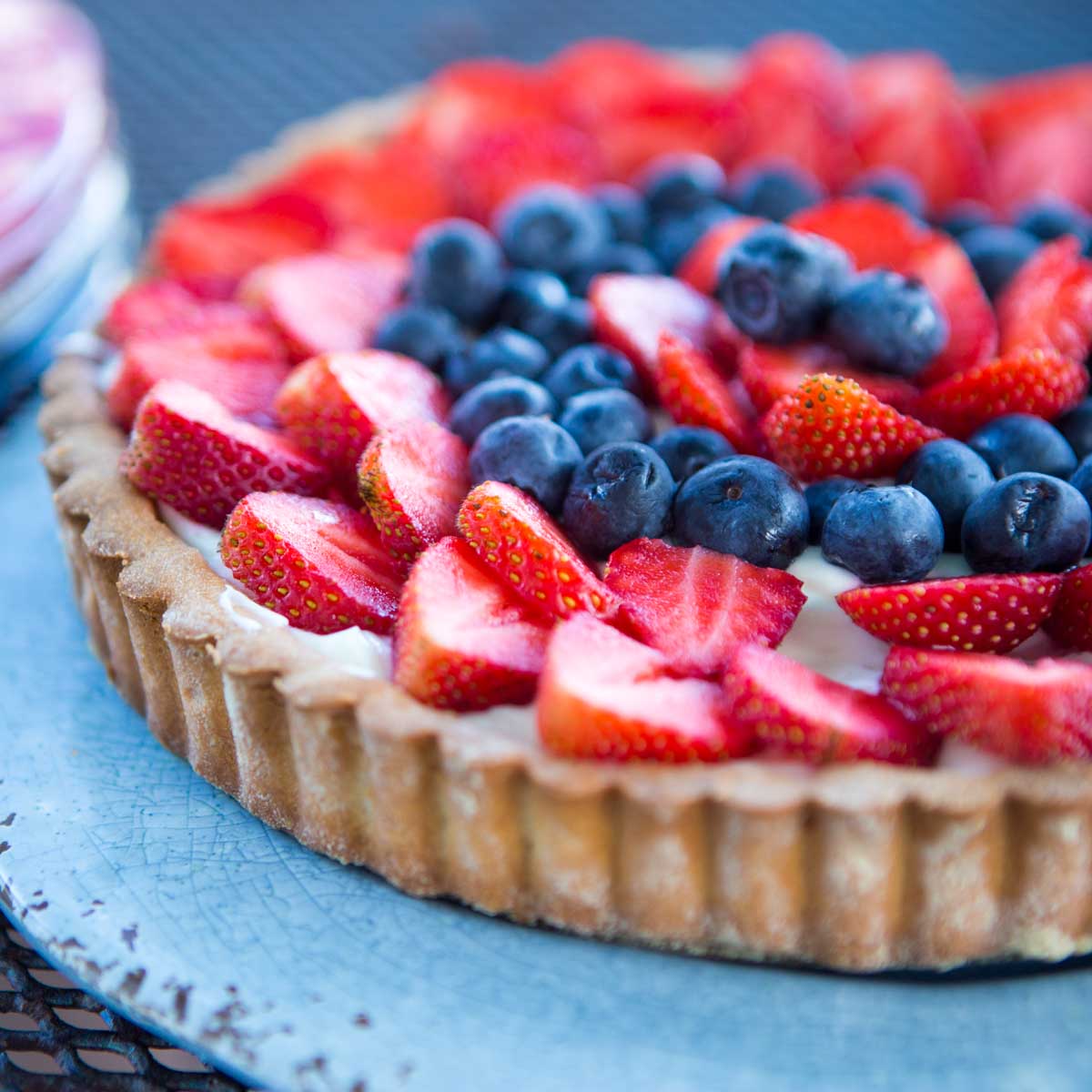 A blue plate with a strawberry tart featuring a cookie crust, creamy filling, and fresh summer berries in a red and blue pattern on the top.