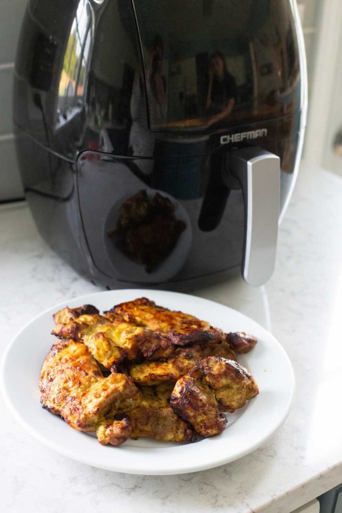 A plate of cooked tandoori chicken sits in front of the air fryer.
