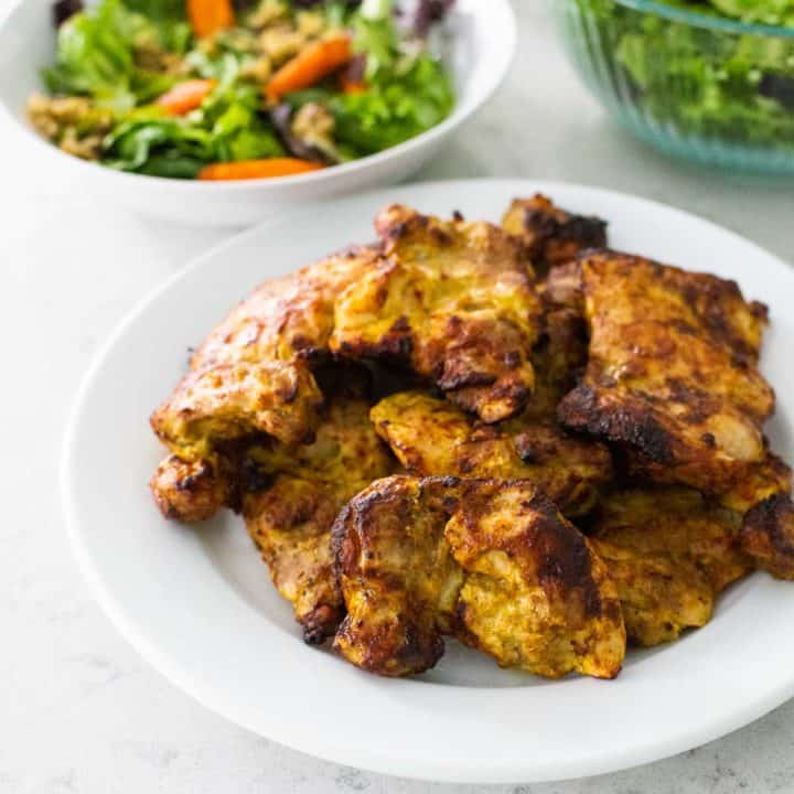 Air Fryer Tandoori Chicken on a white plate. Salad sits in the background.