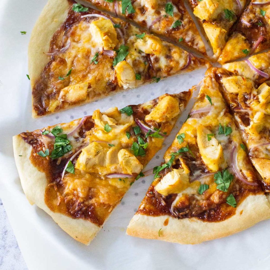 A baked BBQ chicken pizza has been sliced for serving.