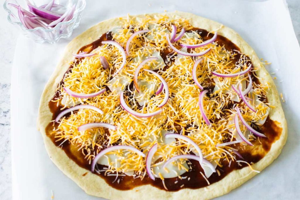 Step 3: Shredded cheddar cheese and sliced red onions are scattered across the top of the pizza.
