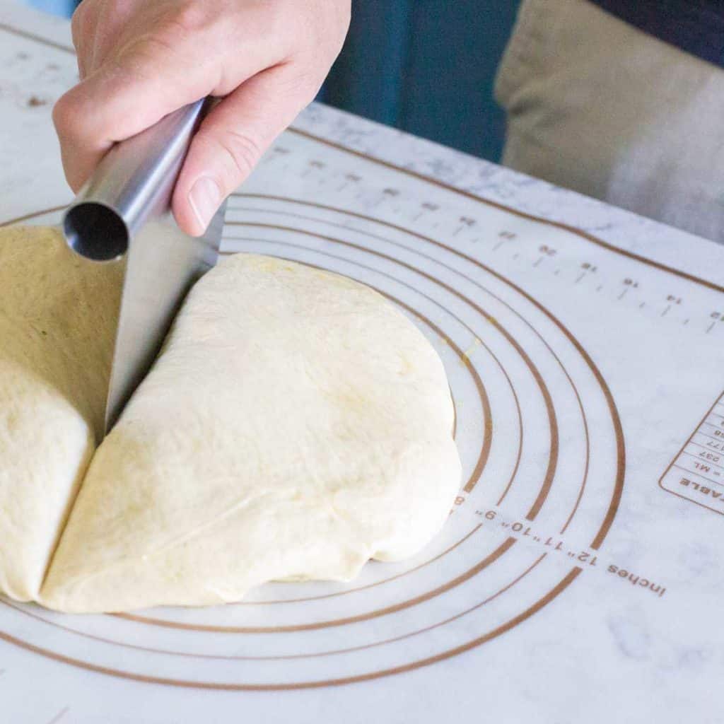 A hand divides pizza dough with a pastry scraper.