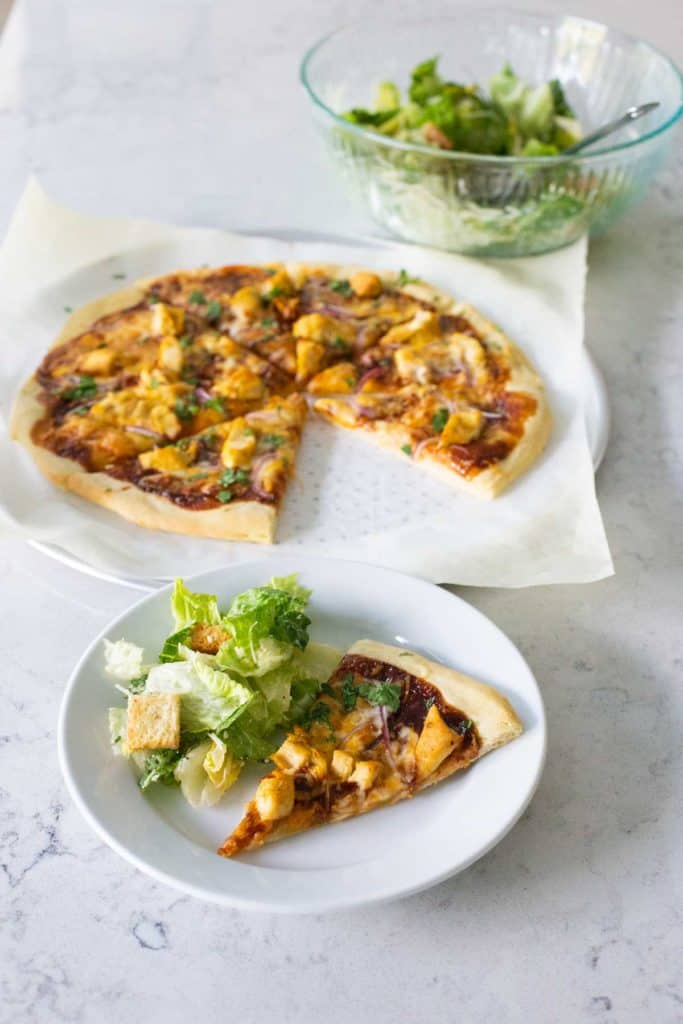 A finished pizza has been sliced and served with a caesar salad.