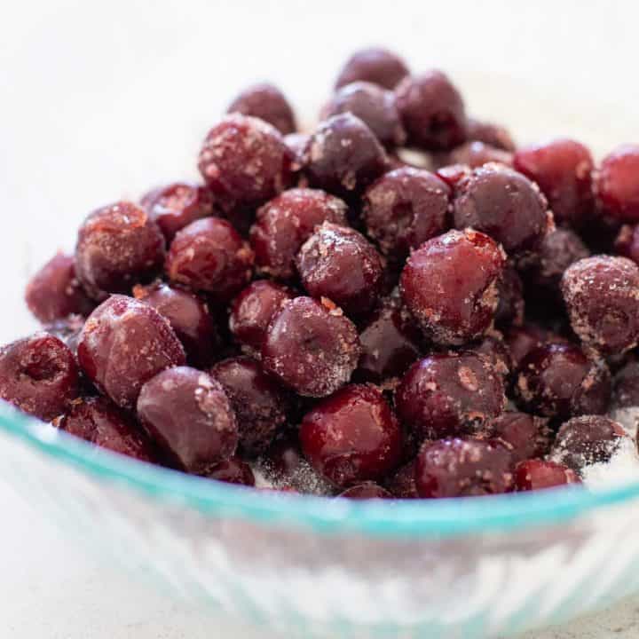 A mixing bowl filled with pitted, frozen cherries.