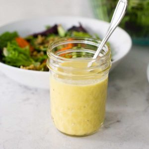 A mason jar filled with lemon parmesan vinaigrette sits in front of a salad.