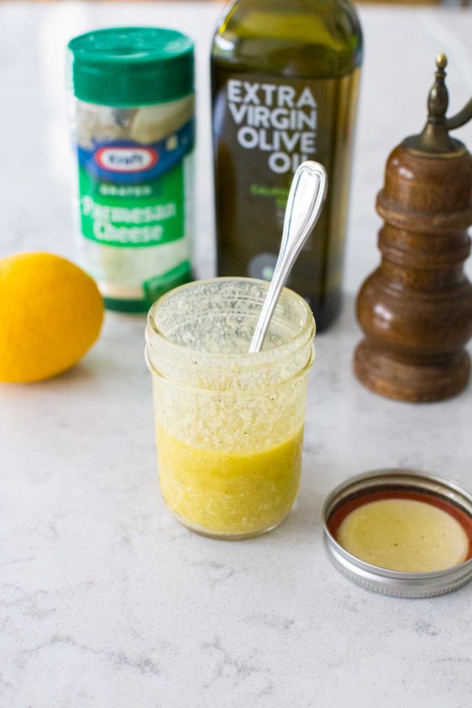 Lemon parmesan vinaigrette in a mason jar sits in front of the ingredients.