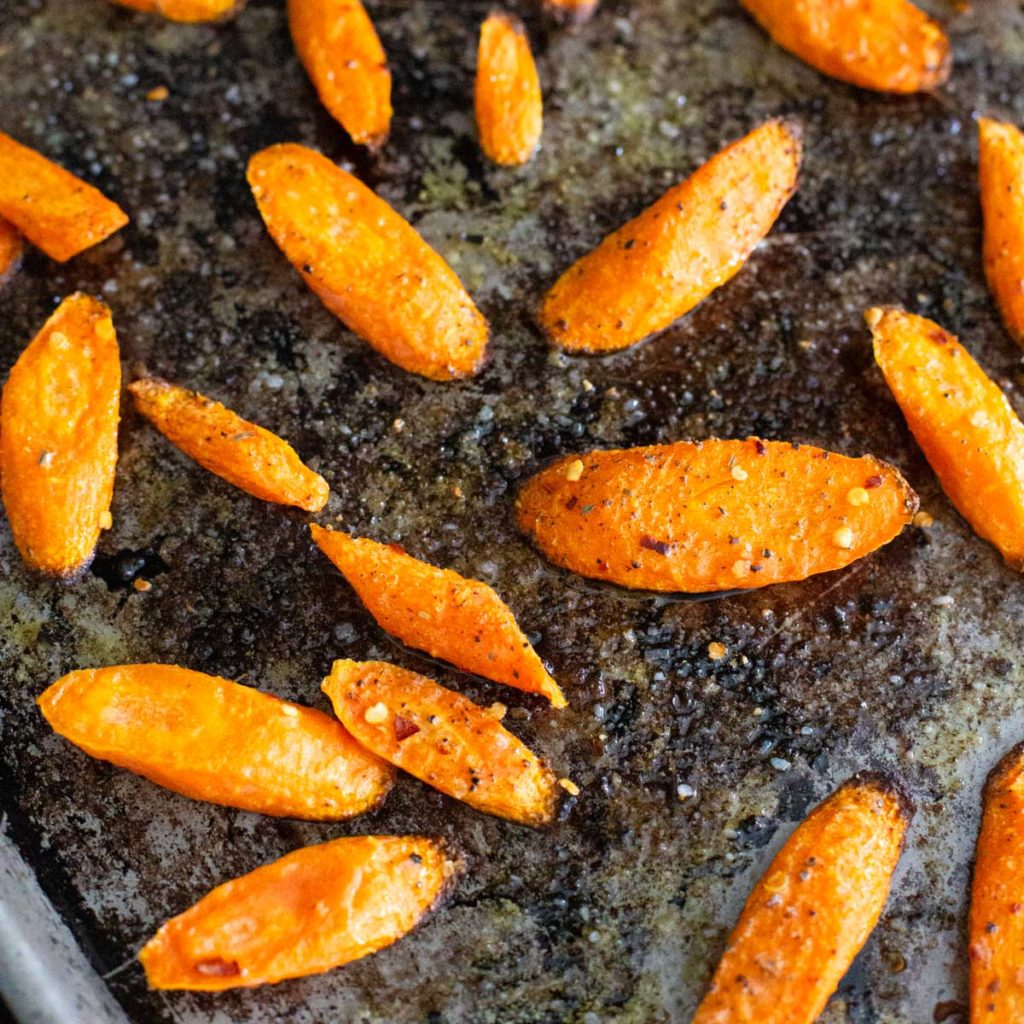 A roasting pan has crisped roasted carrots sprinkled with seasonings.