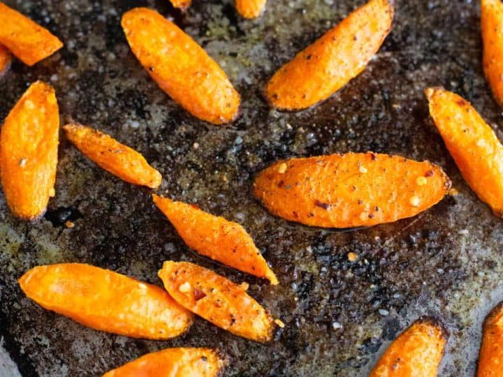 A roasting pan has crisped roasted carrots sprinkled with seasonings.