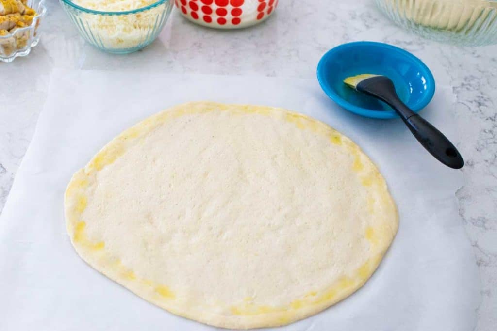 A fresh pizza dough crust is brushed with olive oil before topping.