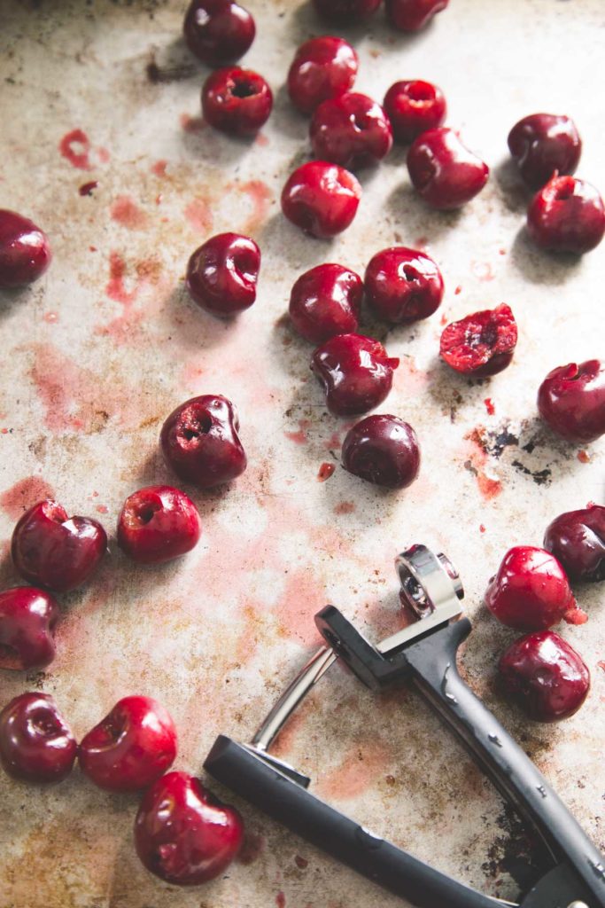 A cherry pitter sits on a tray next to fresh cherries.