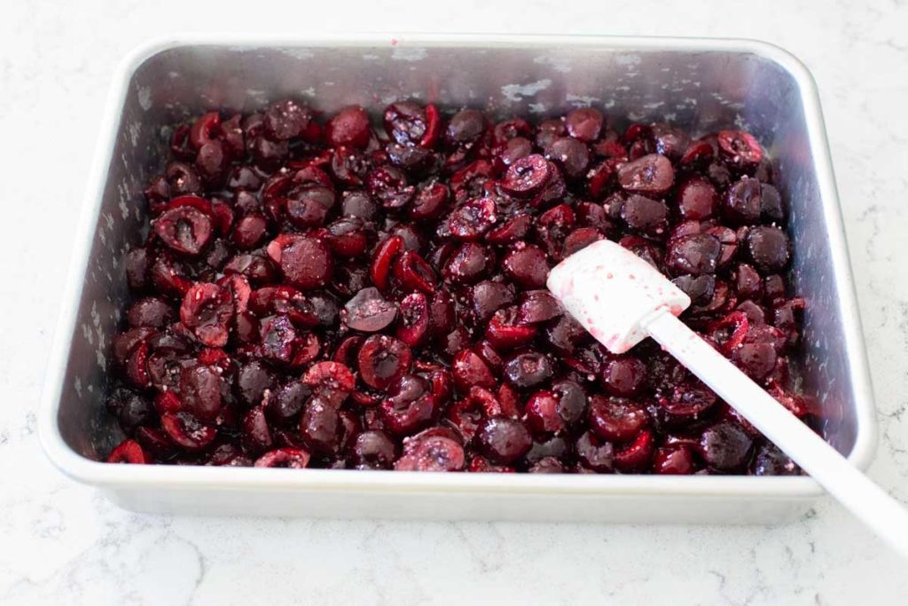 Step 1 of assembling the cherry crisp: The fresh cherries are added to the baking pan and spread into an even layer.