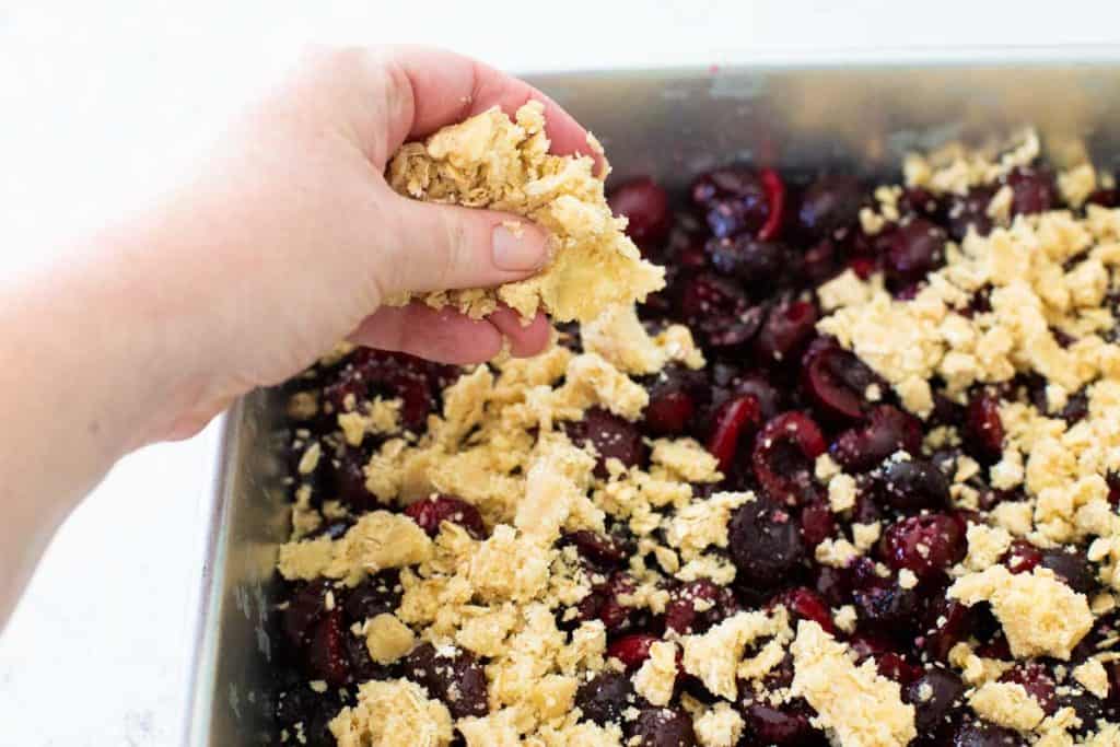 A hand is showcasing how to pinch the crisp topping over the fruit.