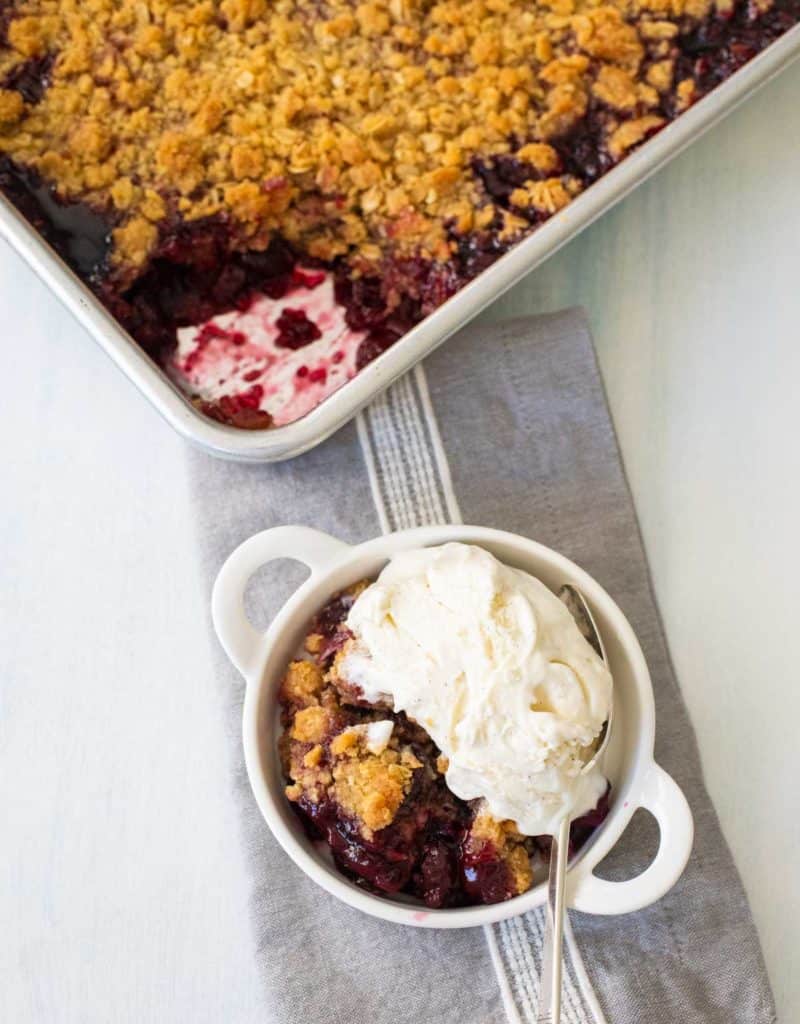 A serving of cherry crisp has a scoop of vanilla ice cream on top.