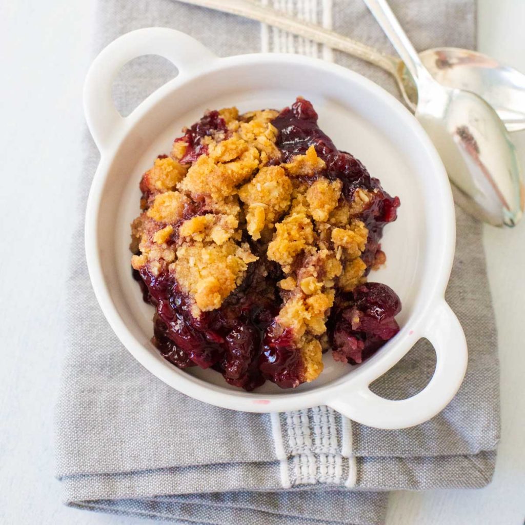 A white bowl of fresh cherry crisp shows the juicy filling and golden brown crumble topping.