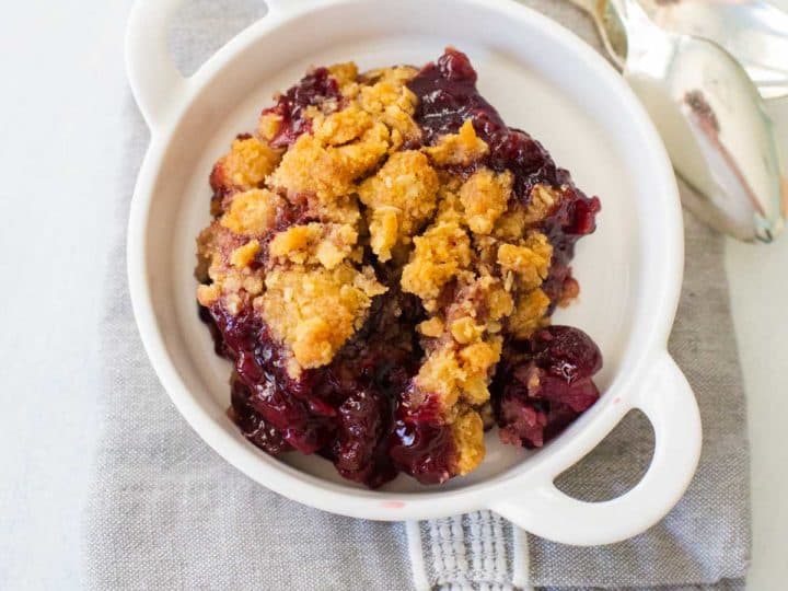A white bowl of fresh cherry crisp shows the juicy filling and golden brown crumble topping.