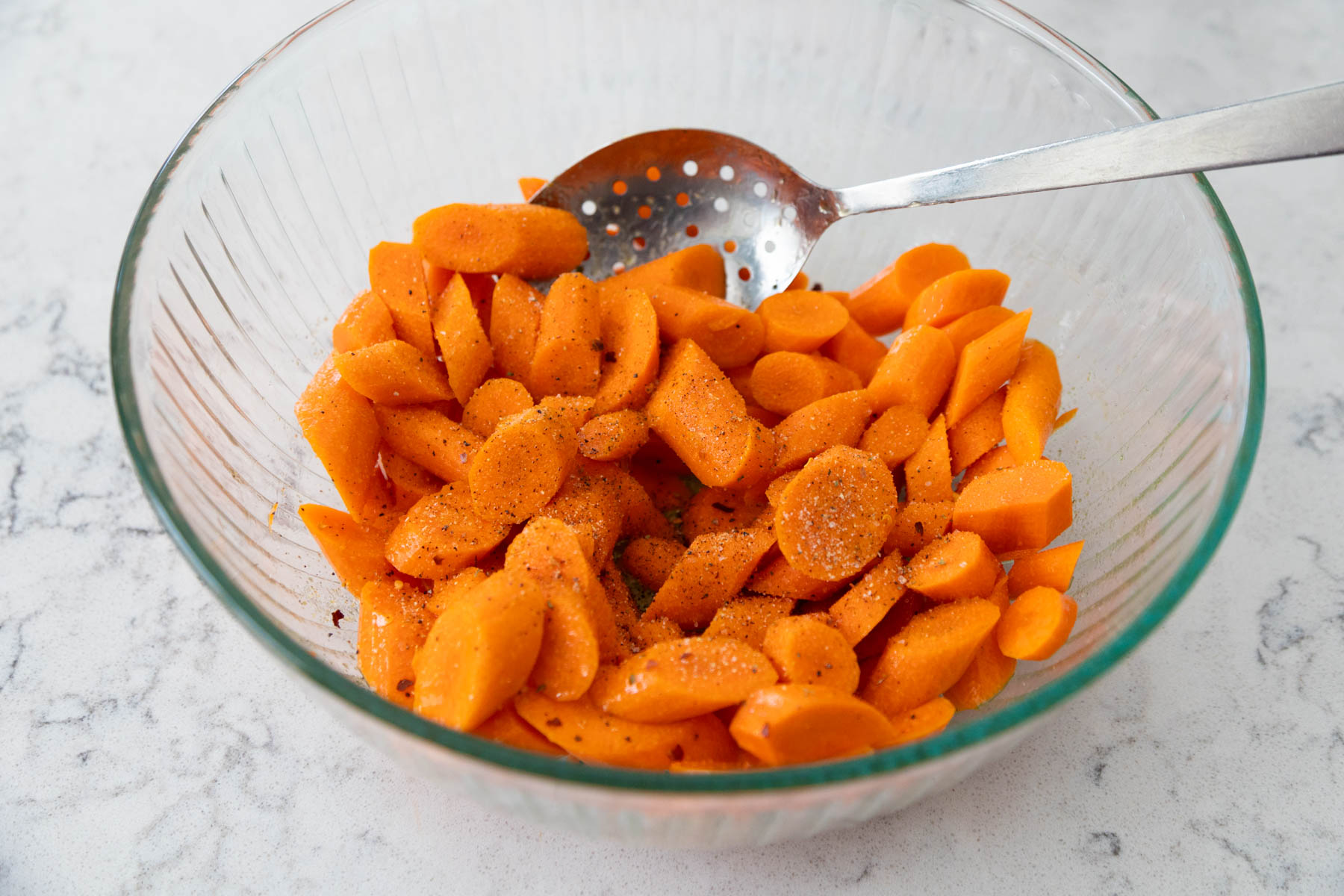 The sliced carrots are in a large mixing bowl being stirred with a spoon.