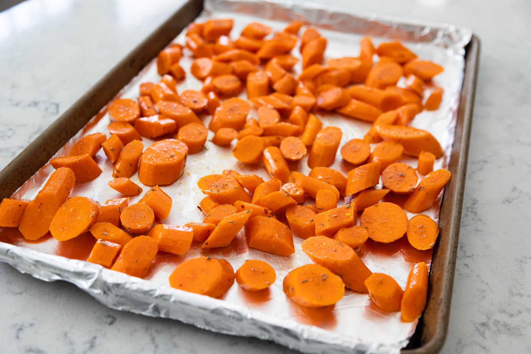 The carrots are on a large baking sheet and tossed with olive oil.