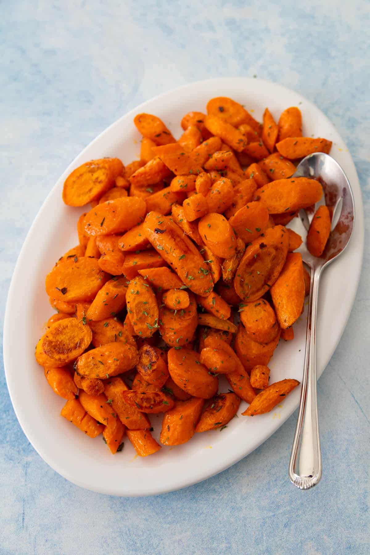 The white platter is filled with the roasted carrots and has a spoon on the side.