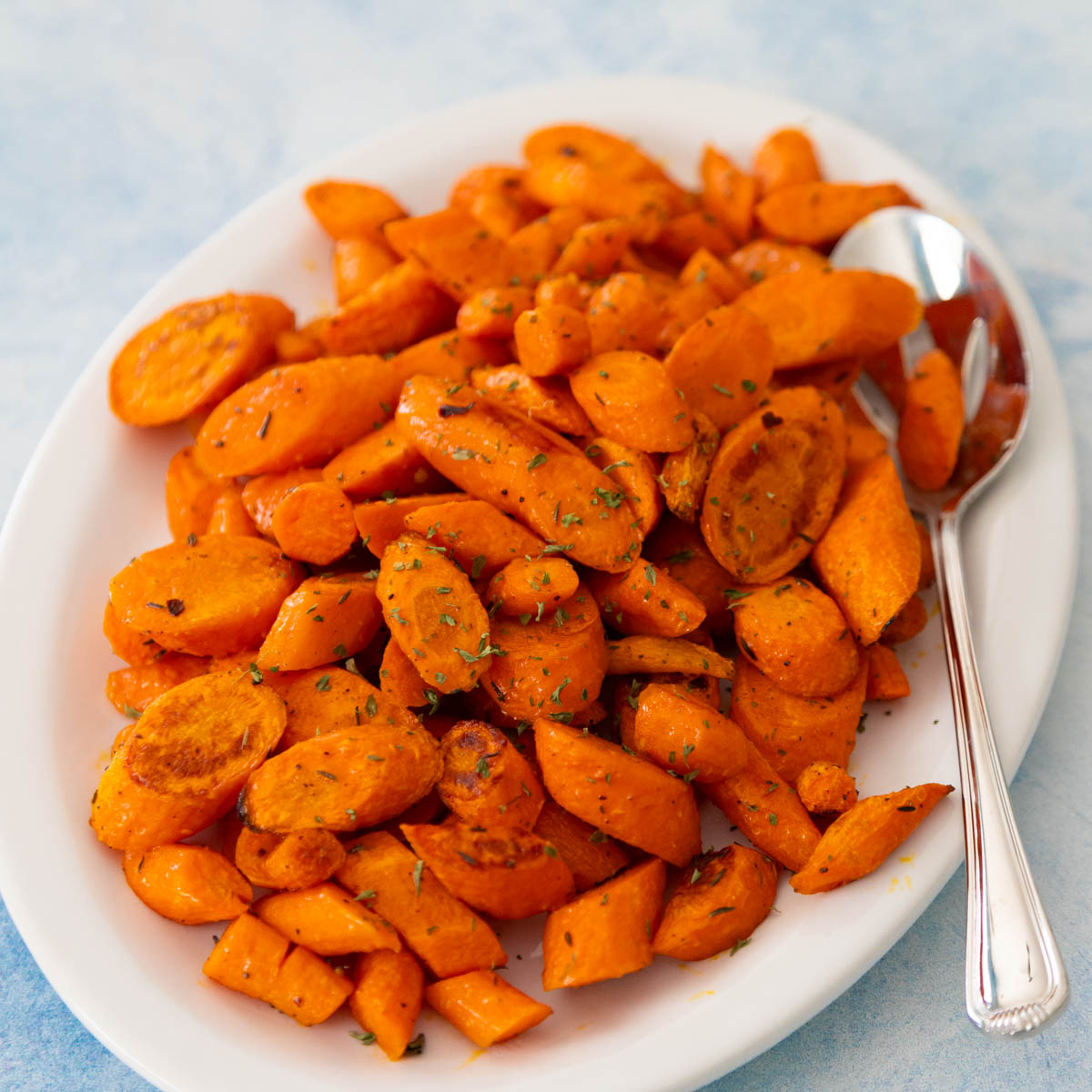 The oven roasted carrots have golden brown edges and are being served on a white platter with a serving spoon.