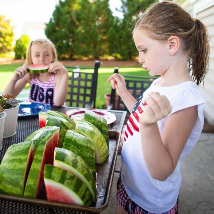 A young girl picks a slice of watermelon from a tray in the backyard.