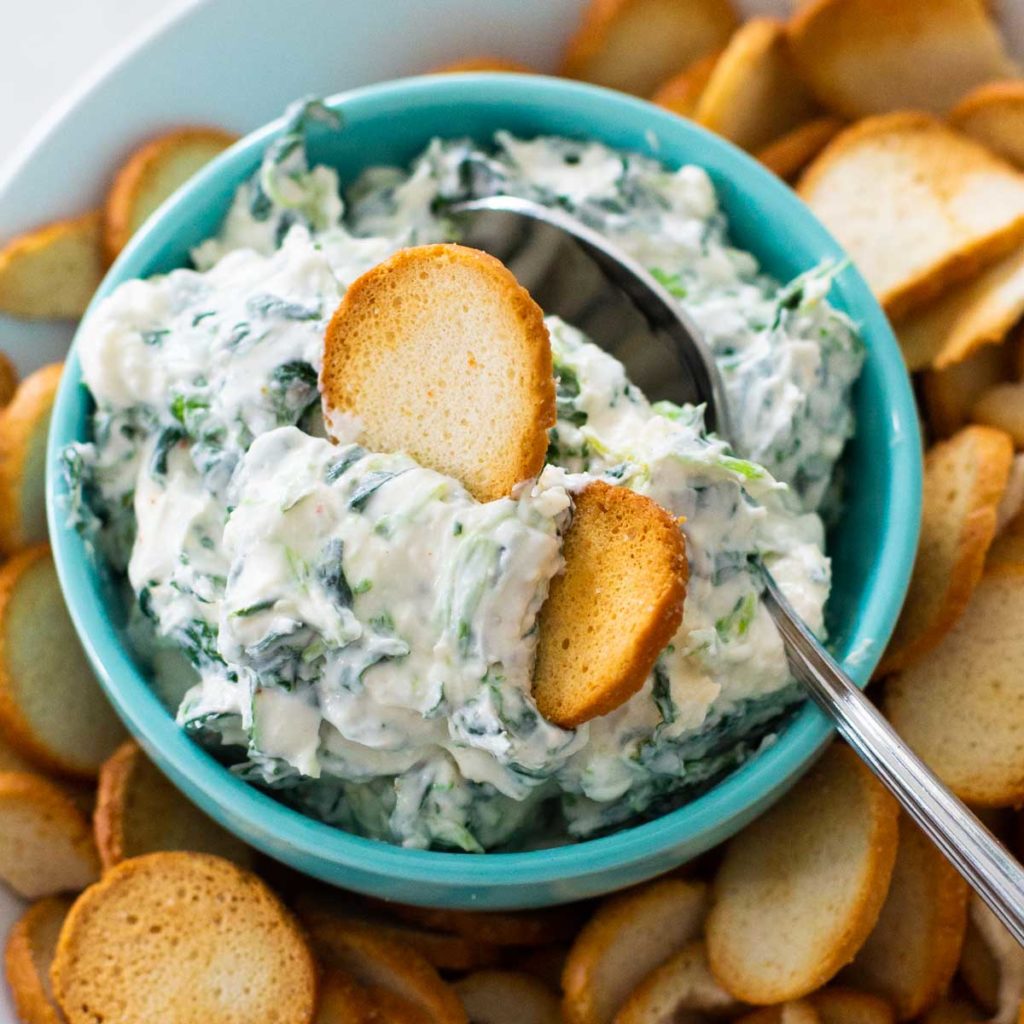 A bowl of cold spinach dip is served with bagel chips for dipping.