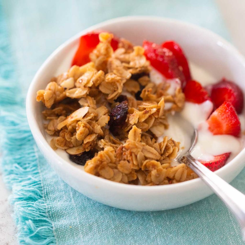 A bowl of yogurt topped with homemade granola and fresh strawberries sits on a blue napkin.