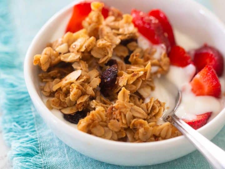 A bowl of yogurt topped with homemade granola and fresh strawberries sits on a blue napkin.