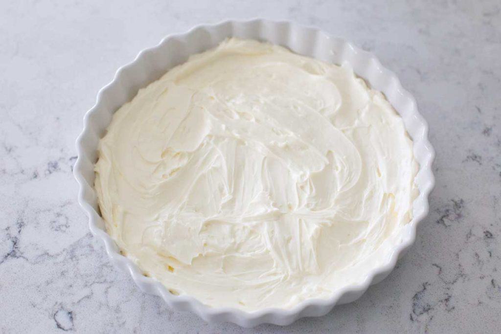 A pie plate has the cream cheese base spread out for the layer dip.