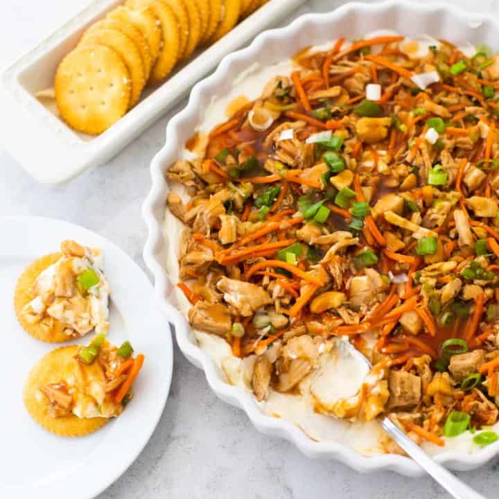 A plate of layered Asian dip is served next to butter crackers.