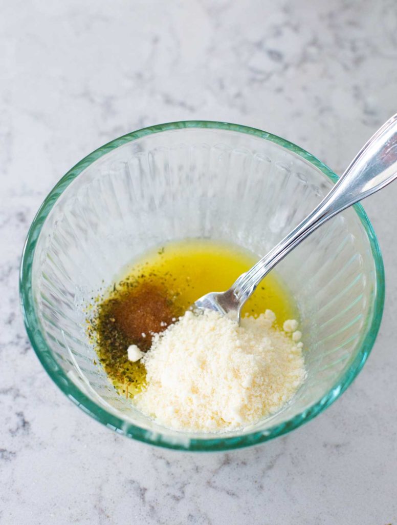 A mixing bowl has melted butter, parmesan cheese, and seasonings ready for blending.