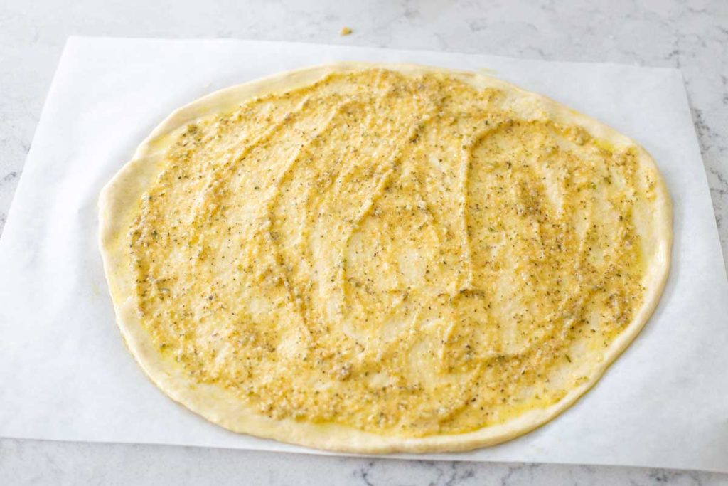 A pizza dough has been rolled out and topped with a garlic butter sauce.