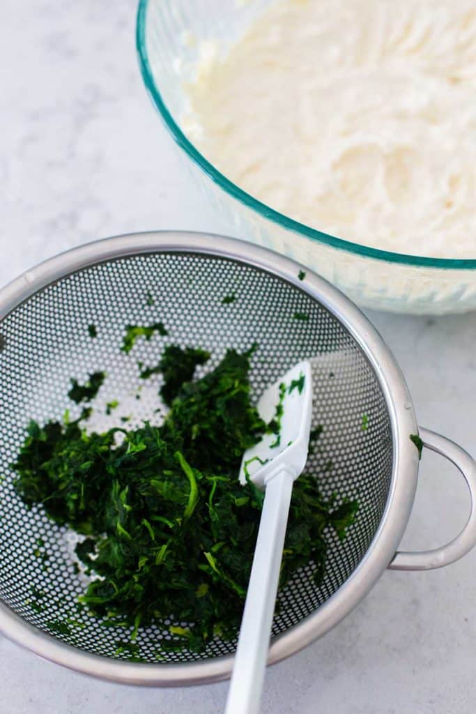 Drained spinach in a colander with a spatula.