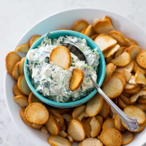 A bowl of spinach dip is served with bagel chips for dipping.
