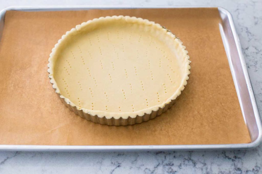 A prepared tart shell is on a baking sheet ready for the treacle tart filling.