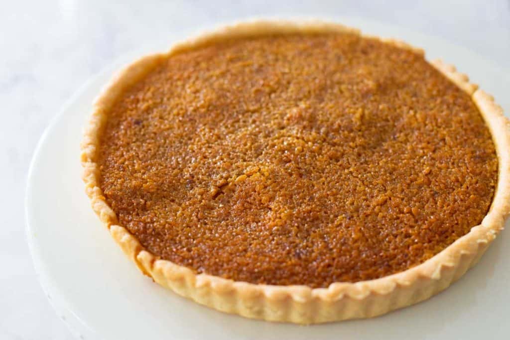 The finished treacle tart is on a cake plate.