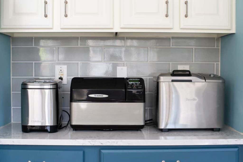 Three bread makers sit on a kitchen counter.