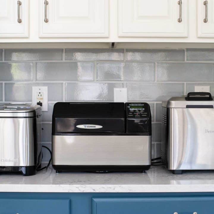 3 bread makers sit on a kitchen counter.