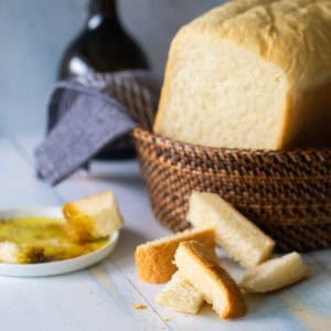 A loaf of bread machine Italian bread sits in a basket next to a few sample wedges near a plate of olive oil for dipping.