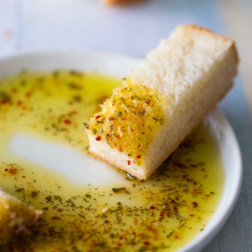 A wedge of Italian bread is dipped into a plate of seasoned olive oil.