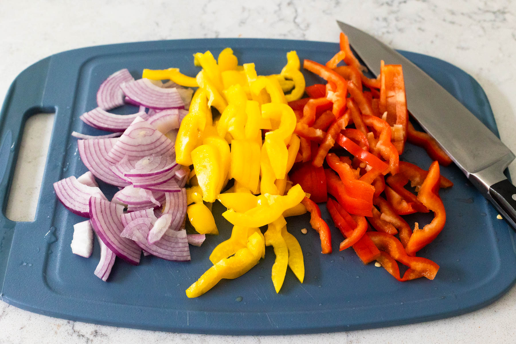 The red onion and bell peppers have been sliced on a cutting board.