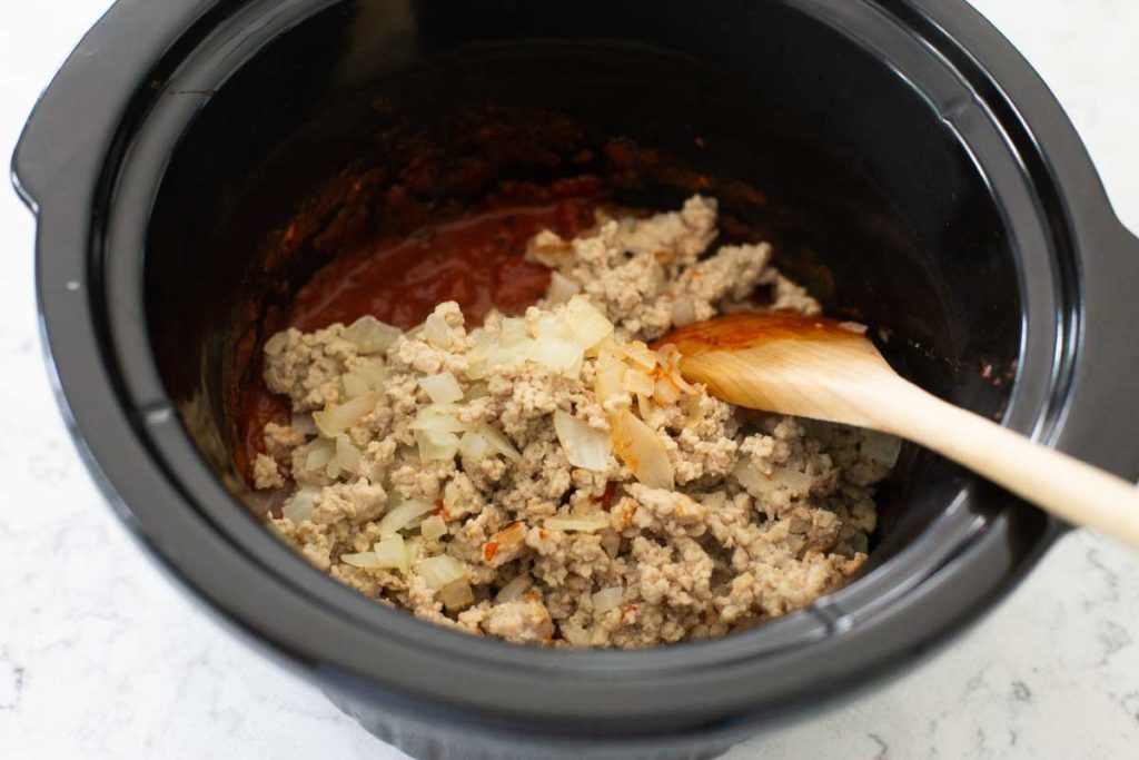 Browned ground chicken and a chopped onion are added to the sauce in the crockpot.