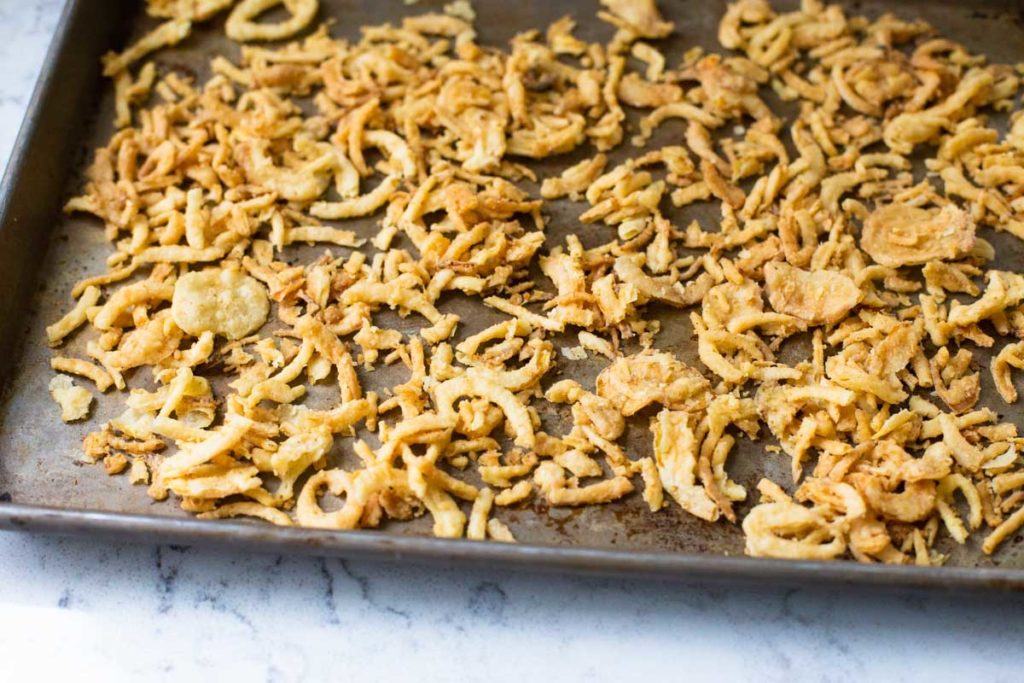 Fried onions are spread on a baking sheet for the oven.