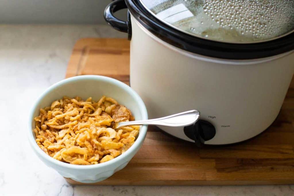 A bowl of fried onions sits next to a crockpot.