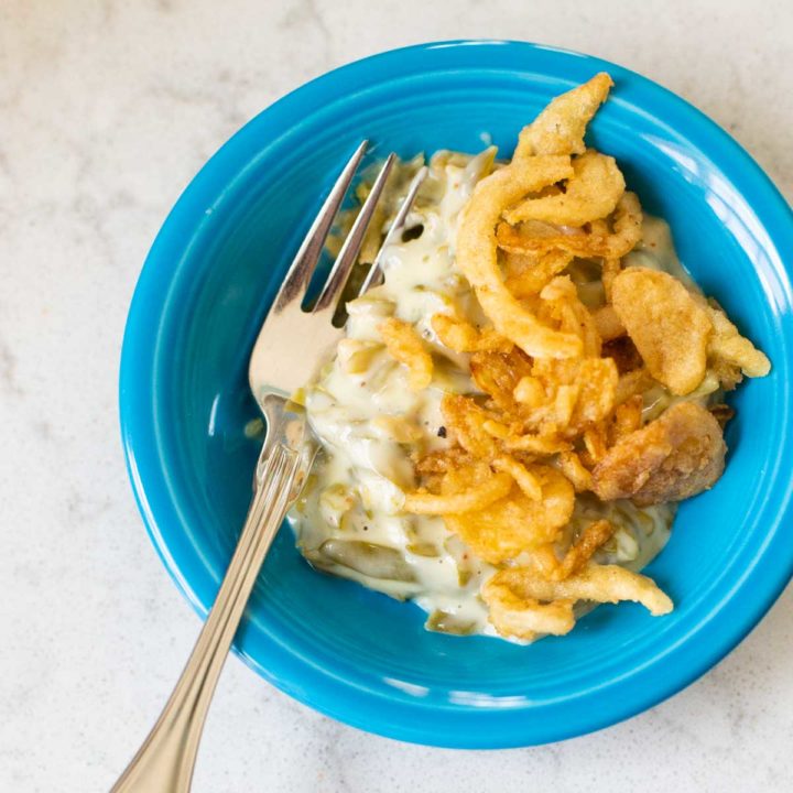 A serving of crispy green bean casserole is in a blue dish with a fork.