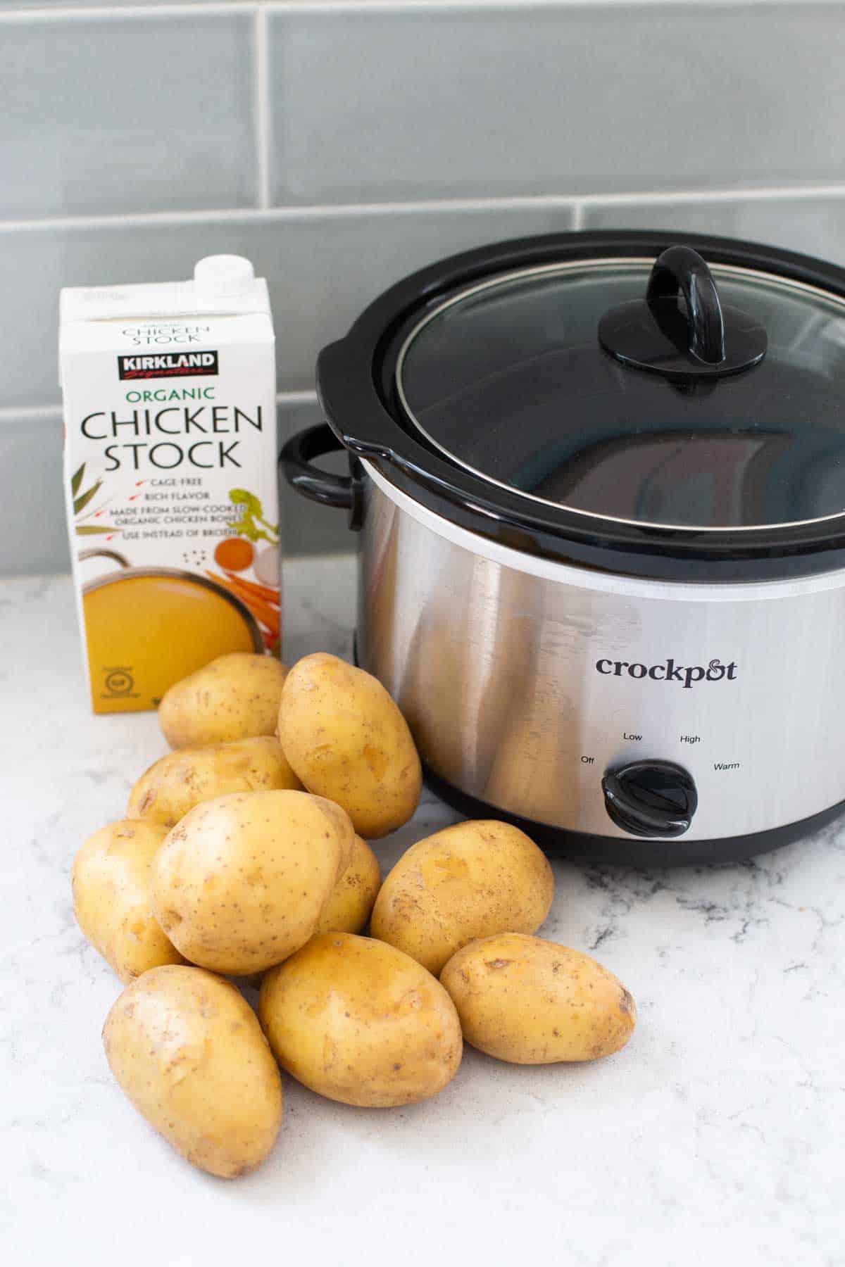 The ingredients for Crockpot mashed potatoes are on a kitchen counter next to a slowcooker.