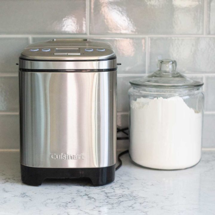 A Cuisinart compact bread maker sits on a kitchen counter next to a jar of flour.