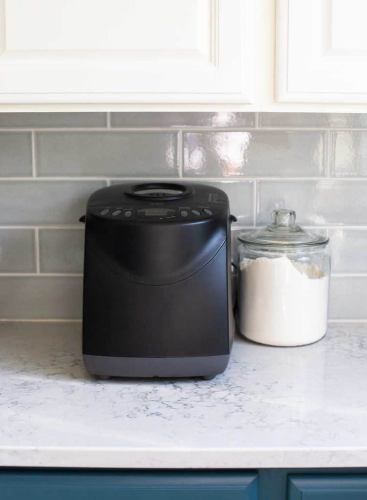 The Hamilton Beach Bread Maker sits on a kitchen counter underneath a cabinet.