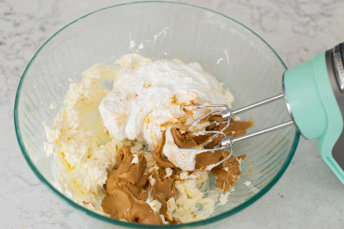 The large mixing bowl has the whipped cream cheese, peanut butter, and marshmallow fluff about to be beaten by a hand mixer.